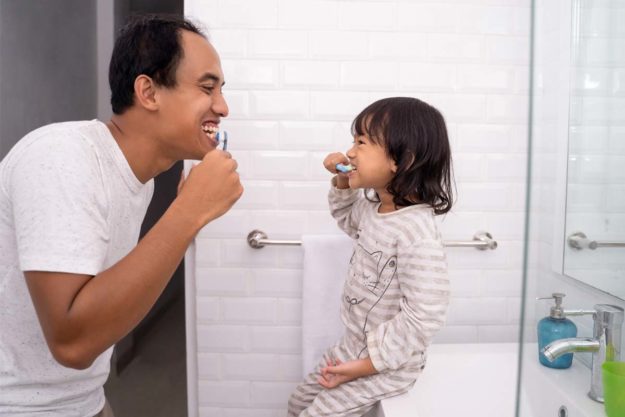 when-should-a-child-go-to-the-dentist (1) father brushign teeth with daughter learning when should a child go to the dentist